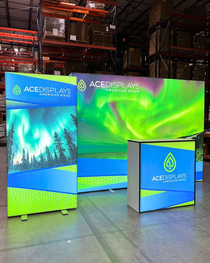 Lumos displays with Ace Display logos are set up on the Ace Displays warehouse floor. There is a large backlit display, a backlit counter in front of it and a backlit banner stand to the left of it.