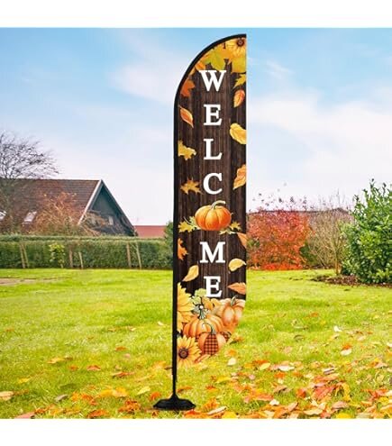 An outdoor flag with a pumpkin patch welcome graphic placed on a yard of green grass and a house in the background.