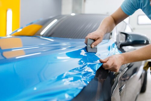 A person wrapping a vehicle in a blue color.