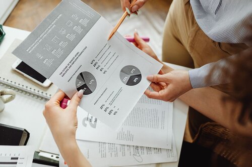 People's hands looking at a sheet of paper with analytics and charts on it. 