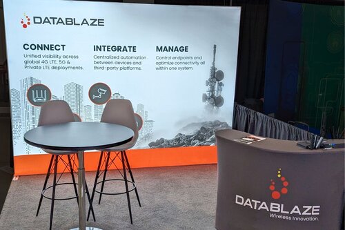 DataBlaze 10x10 booth with backdrop showing 'Connect, Integrate, Manage' pillars illustrated with cityscape and tower graphics, high-top table with stools, and branded reception counter with orange accent stripe