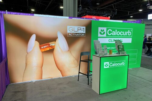 Trade show booth by Ace Displays for Calocurb. Features a Lumos display with green graphics and a product image, and a Lumos counter at a trade show.