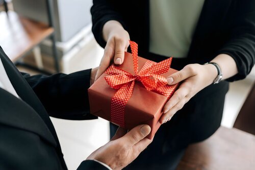 Professional businesspeople exchanging a red gift box with polka dot ribbon in an office setting