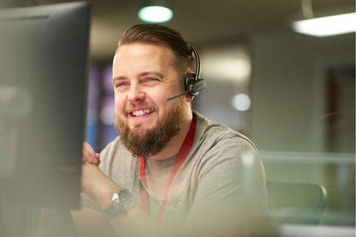 Customer service team member smiling at the computer with a headset on.