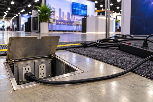 In-ground outlet with extension cord plugged in and other various outlets being used in a busy Trade Show venue