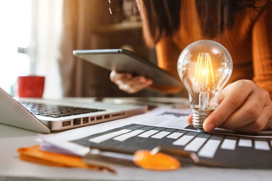 Person holding a light bulb while looking at a tablet and laptop