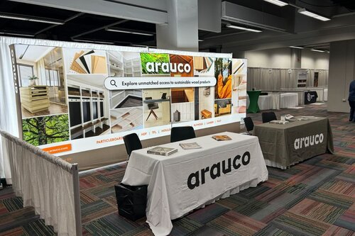 Arauco's trade show booth with a backlit display and two branded tables in front of it. One table cover is white with a black logo and the farther table cover is grey with a white logo. There are pamphlets on the tables and the display has a search-engine graphic.