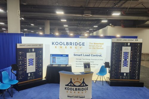 Koolbridge's trade show booth with a backlit flat display with a branded podium in front of it. Energy products to the left and right of the display. There is a monitor located in the middle of the display on a small table and a few light blue chairs in front of it as well. There is a blue curtain behind the display.