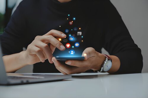 Hands holding a smartphone with glowing social media icons (likes, comments, and follows) floating above the screen.