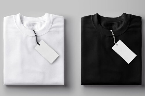 Two folded t-shirts in white and black with blank product tags attached, shown on neutral gray background