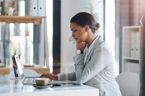 Professional woman in gray business suit working thoughtfully at laptop in modern office, planning trade show strategy