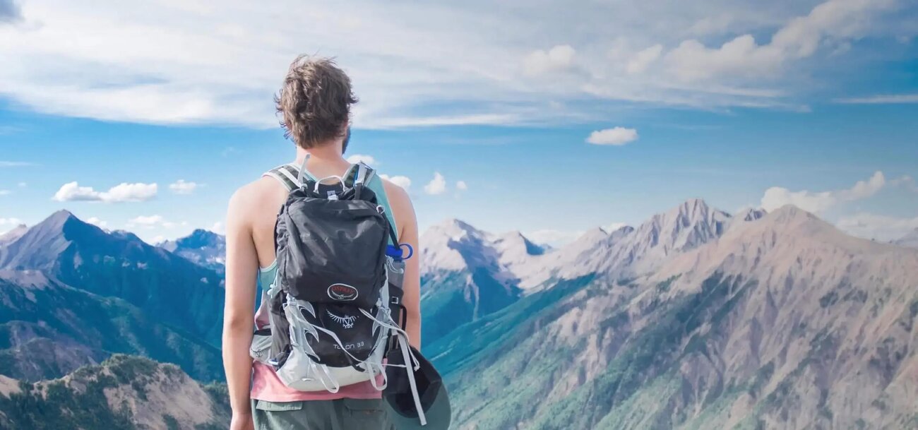 Hiker with a backpack overlooking a mountain landscape, ideal for a travel blog website built with Jimdo.