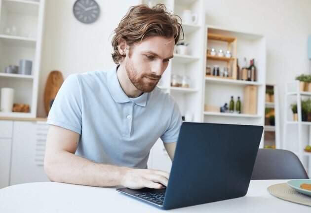 Lächelnde Person in einem Workshop neben einem Monitor, der eine Website mit Möbelentwürfen und einem großen Play-Button-Overlay anzeigt.
