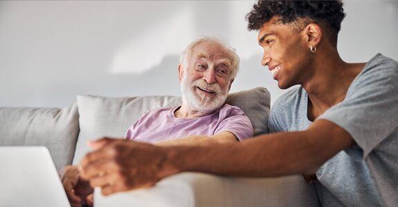 A helper shows off some pretty red flowers to a senior. They're smiling in the kitchen. 