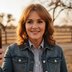A profile picture for Anna, she's smiling towards the camera, with red hair and a jean jacket on. It's golden hour and the sun is behind her while she stands out in a field.