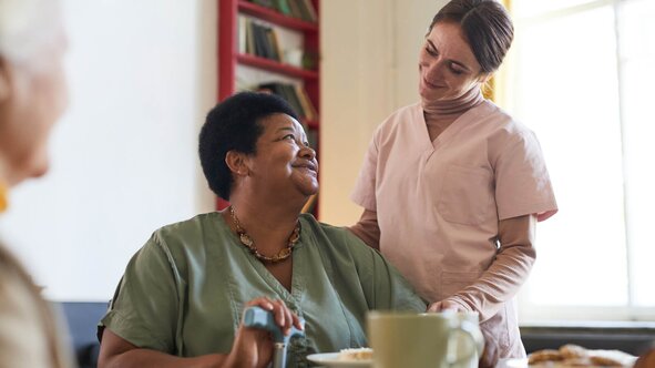 Herewith Helper serving a freshly prepared meal to a smiling senior woman at home, providing meal preparation care.