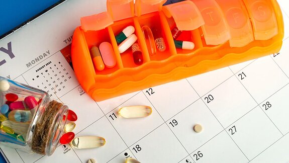 A pill organizer sits on a calendar to help manage daily medications. Consistent reminders and support can improve adherence and health outcomes.