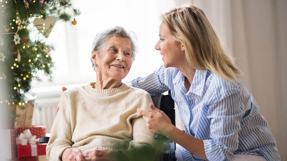 Young Herewith Helper visiting a senior woman beside the Christmas tree, sharing holiday companion care at home.