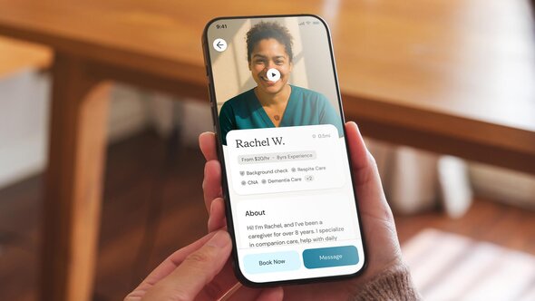 A person holds a smartphone displaying a Helper’s profile with her name, photo, hourly rate, and service badges.
