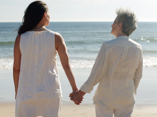 A Helper and senior walk hand in hand along the beach, sharing a peaceful moment. Compassionate in-home care supports independence, connection, and well-being.