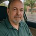 A man sits in the driver’s seat of a car, looking calmly at the camera.