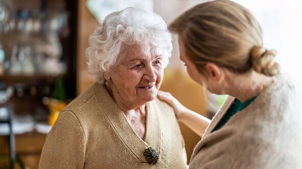 Herewith Helper talking warmly with a senior woman, hand on her shoulder, during a friendly companion care visit.