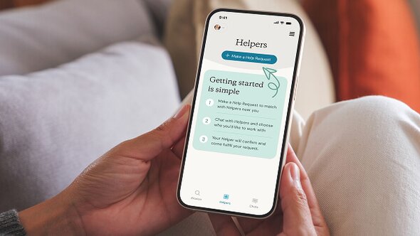 A person holds a smartphone showing the Herewith app screen with instructions on how to request a Helper. The setting is calm and homey, with focus on usability and clarity.