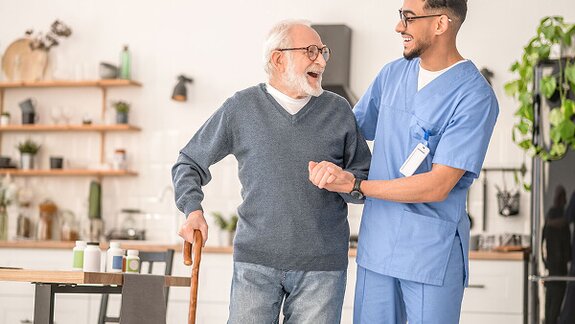A Helper supports a senior with walking during recovery at home. In-home care can help improve mobility, safety, and confidence after a hospital stay.