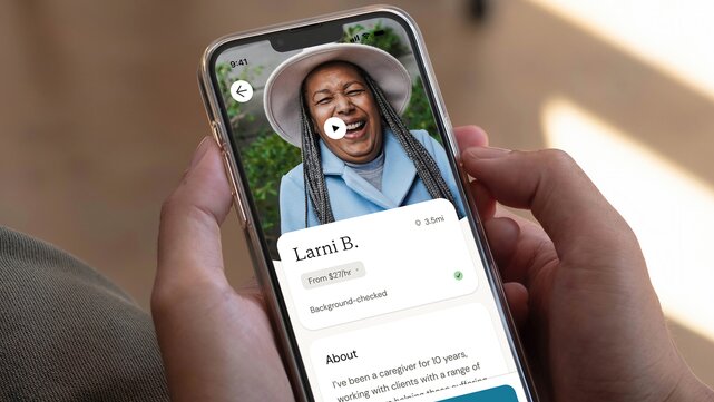 Customer holds a phone showing the profile for a Helper named Larni B. 