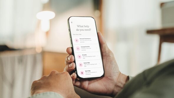 A person holds a phone with the Herewith app open, showing a list of help categories including home help.