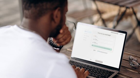 A person uses a laptop to schedule caregiving support through the Herewith website.