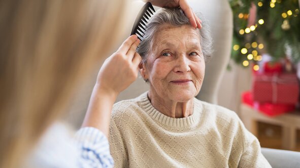 Herewith Helper gently brushing a smiling senior woman's hair at home, providing personal grooming care.