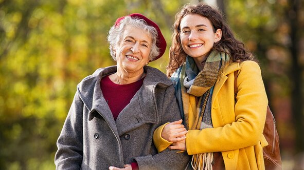 An older woman and her Helper smile arm-in-arm on an autumn day.
