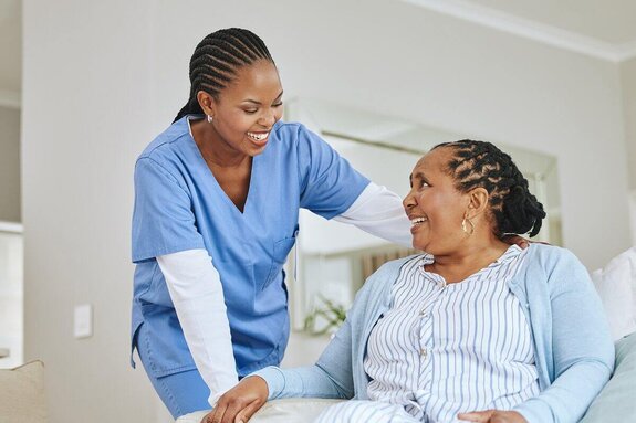 Helper rests a hand on an older woman's shoulder as they smile at each other at home