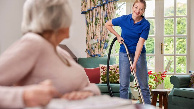 Herewith Helper vacuuming the living room for a senior woman, providing light housekeeping and home care.