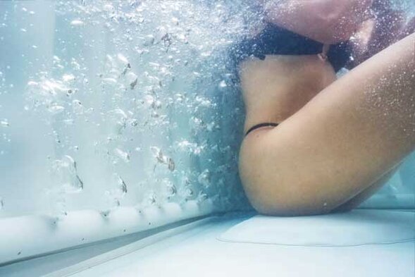 Frau in Badebekleidung sitzt im sprudelnden Wasser eines Whirlpools, Seitenansicht unter Wasser.
