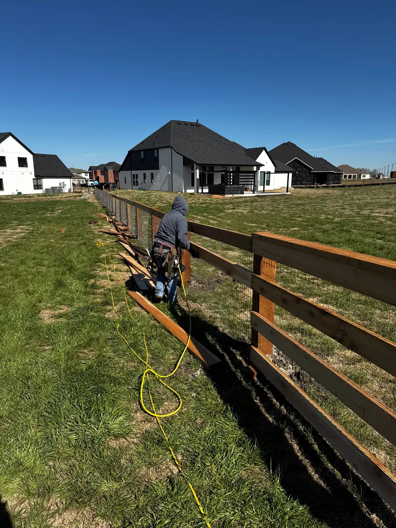 Crew member building a wood rail and wire property fence