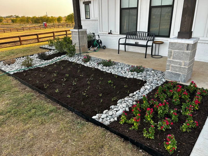 Mulched planting bed with river-rock border along a front porch