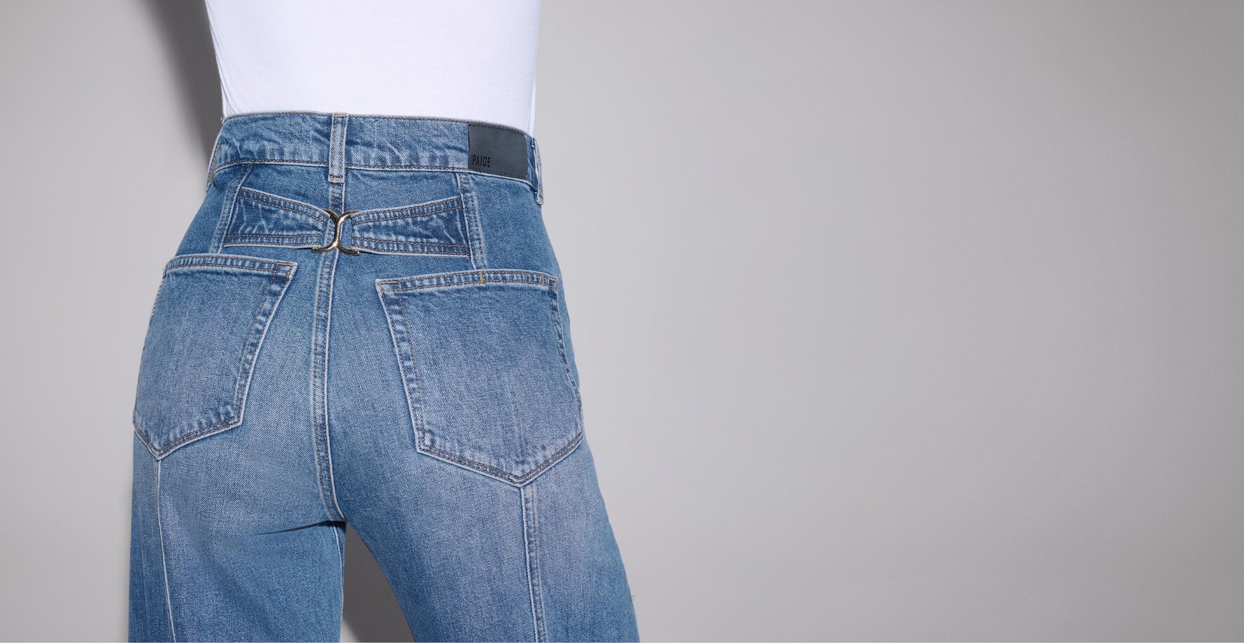 Woman wearing a pair of light wash barrel leg jeans with back seams and a back silver hardware detail