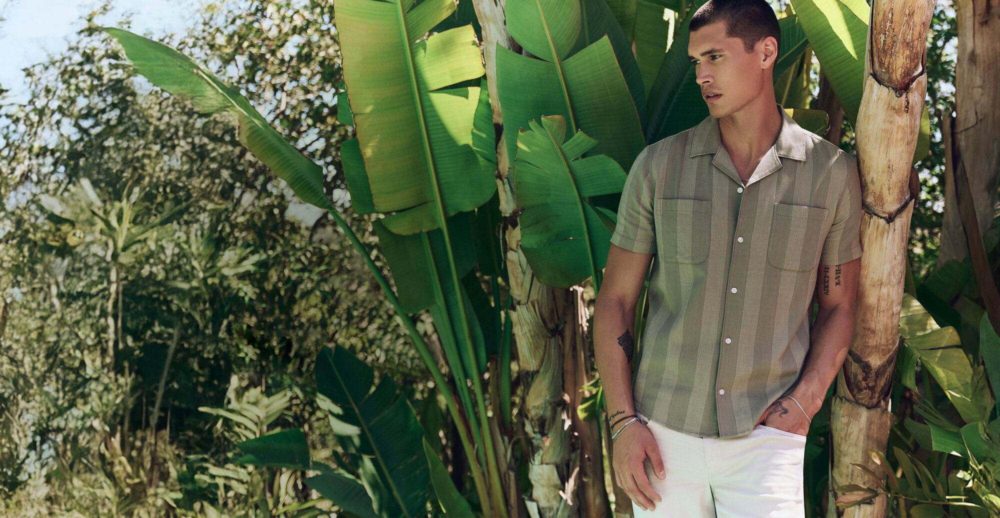 Man wearing a green vertical striped short sleeve shirt with ivory straight leg jeans