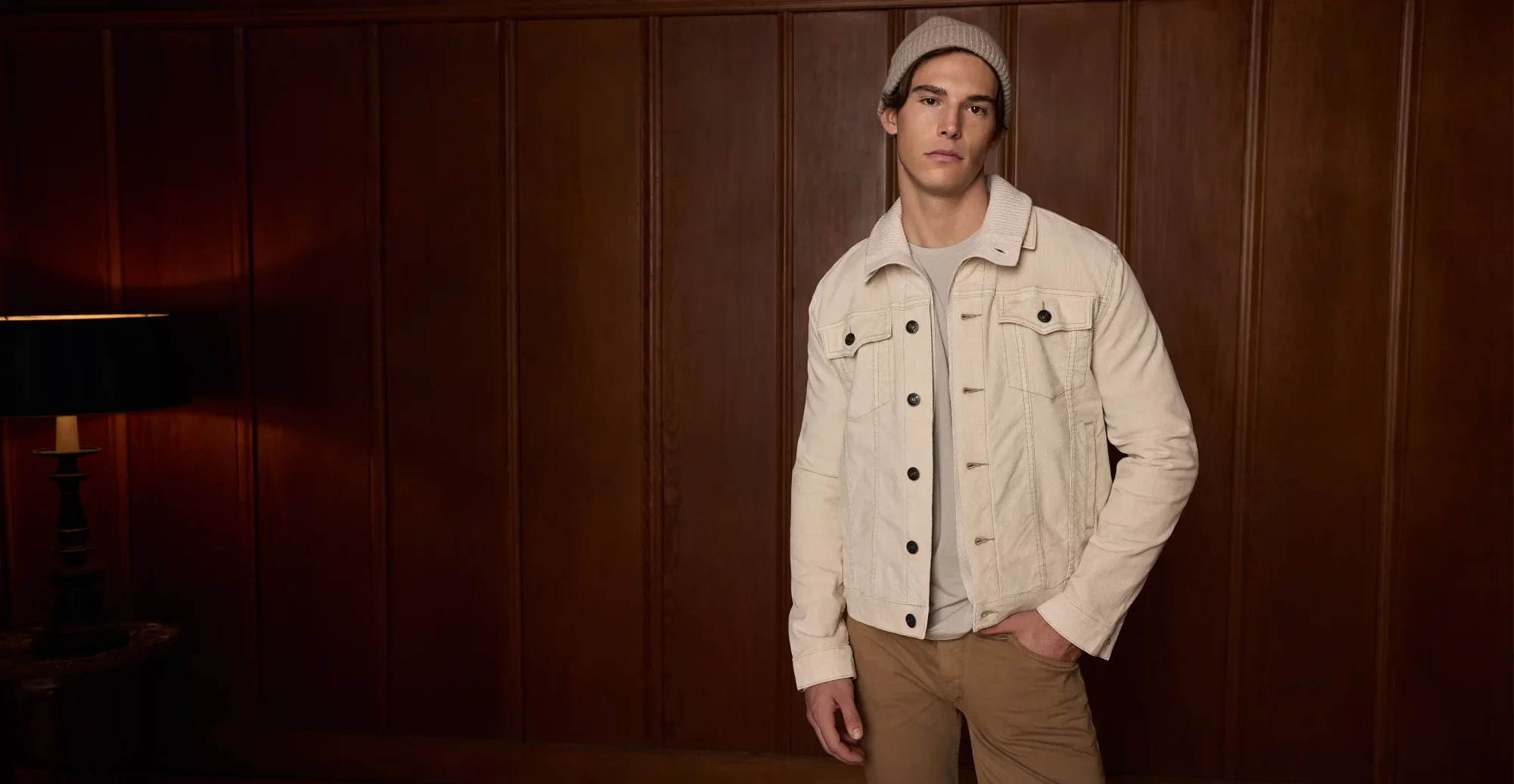 Man standing wearing a sand beanie, ivory corduroy jacket, and khaki pants