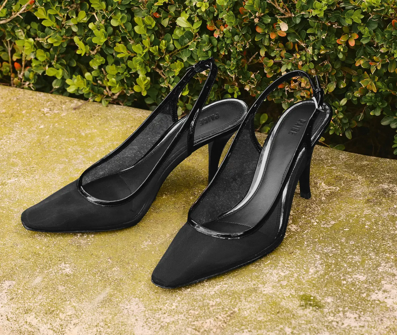 A pair of black mesh pointed toe slingback heels on a mossy green bench