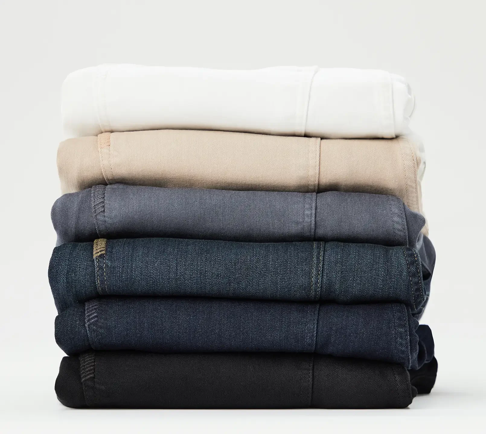 A stack of folded men's denim from lightest washes on top to darkest washes on bottom