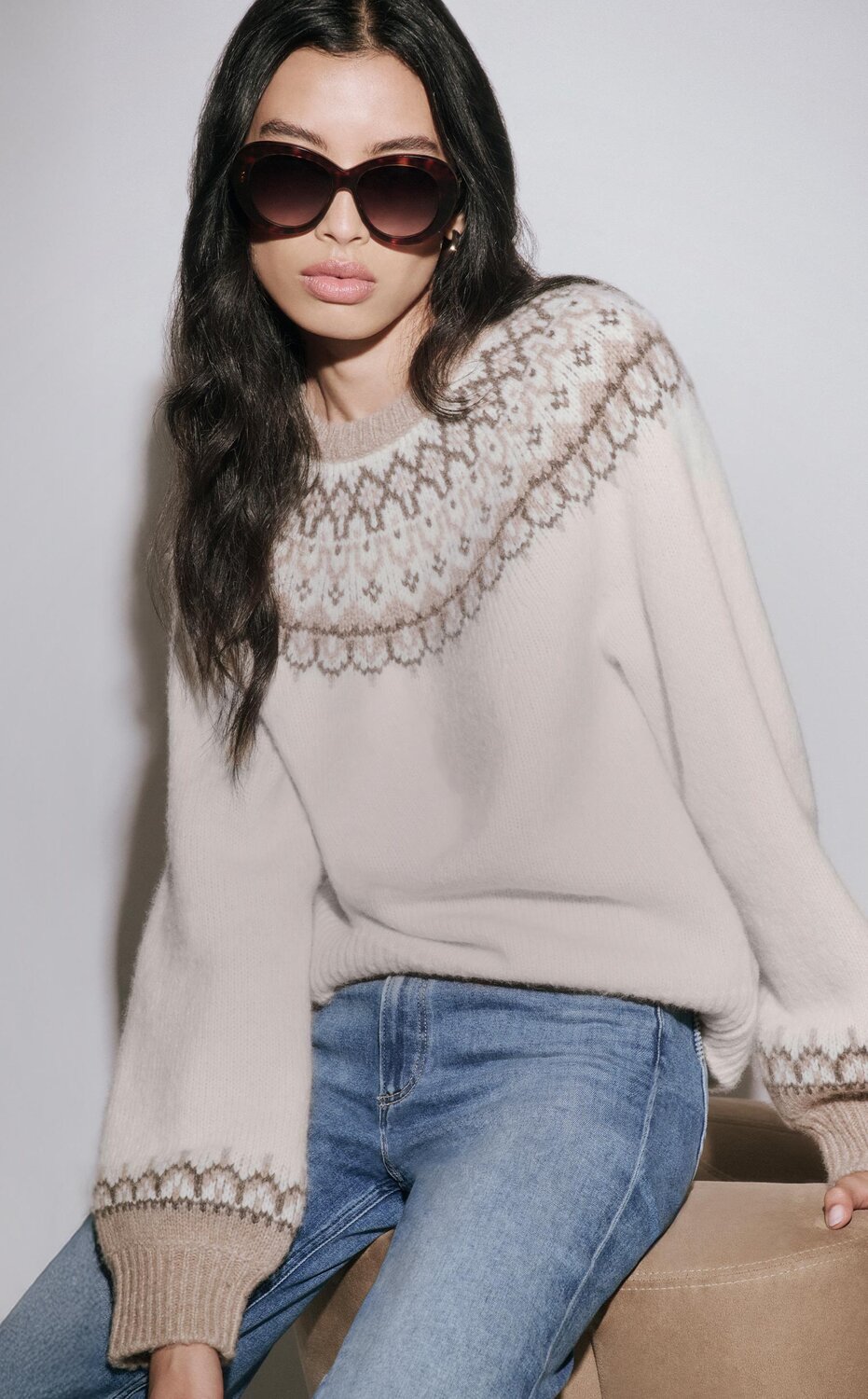 Woman wearing a cream sweater knit dress and tall black boots & woman wearing an ivory fair isle sweater with light wash jeans, oversized sunnies & auburn mules