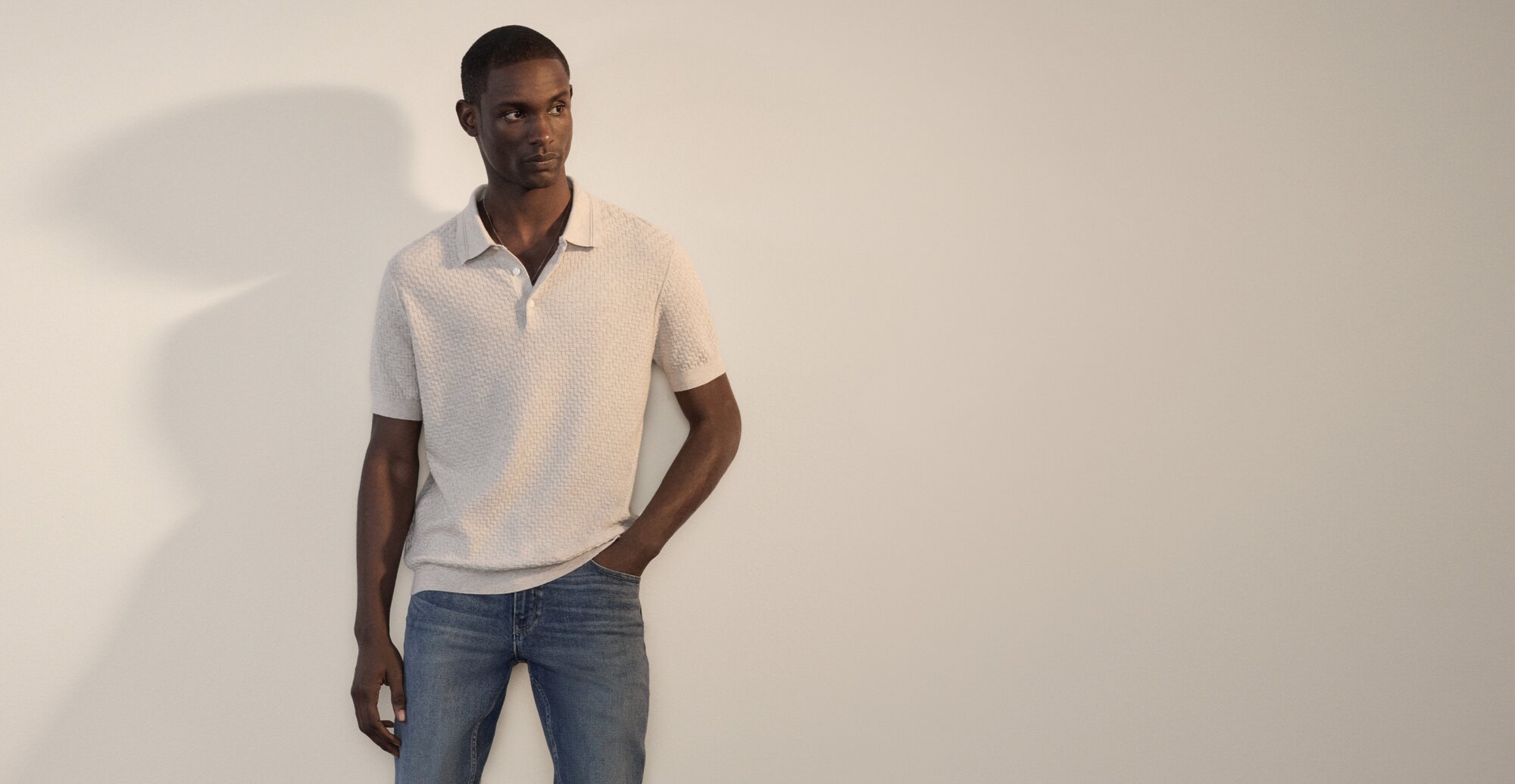 A man wearing a light tan textured short sleeve polo shirt and medium blue denim jeans.