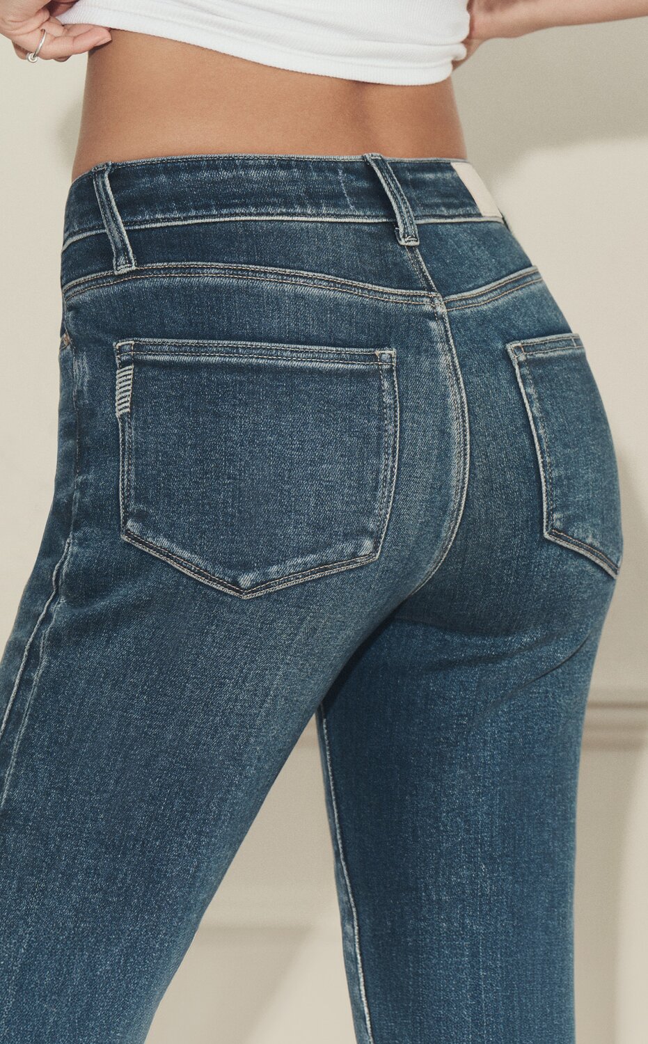 Close-up of a woman wearing PAIGE medium blue wash jeans with signature back pocket detailing.