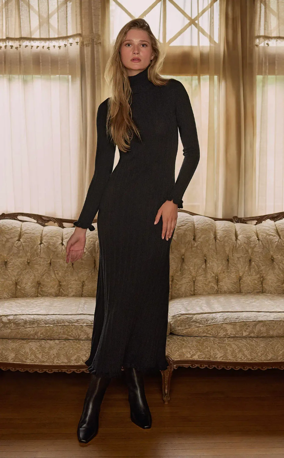 Woman standing inside wearing a long sleeve black midi sweater dress and tall black boots