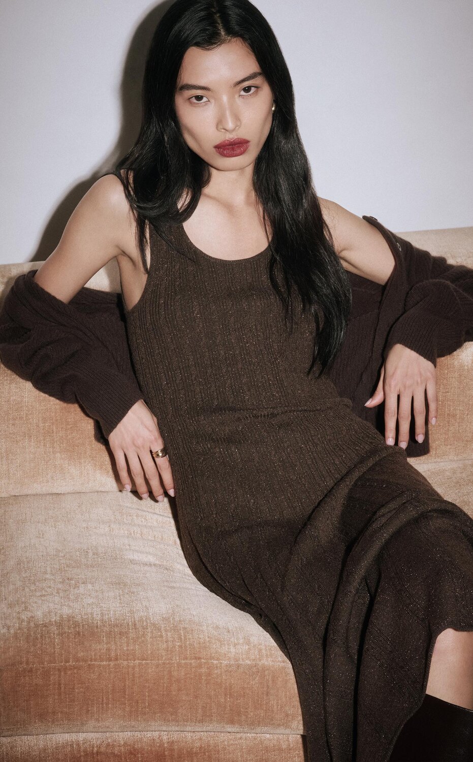 Woman sitting on a couch wearing a long brown sparkle dress with a brown cardigan and tall brown boots