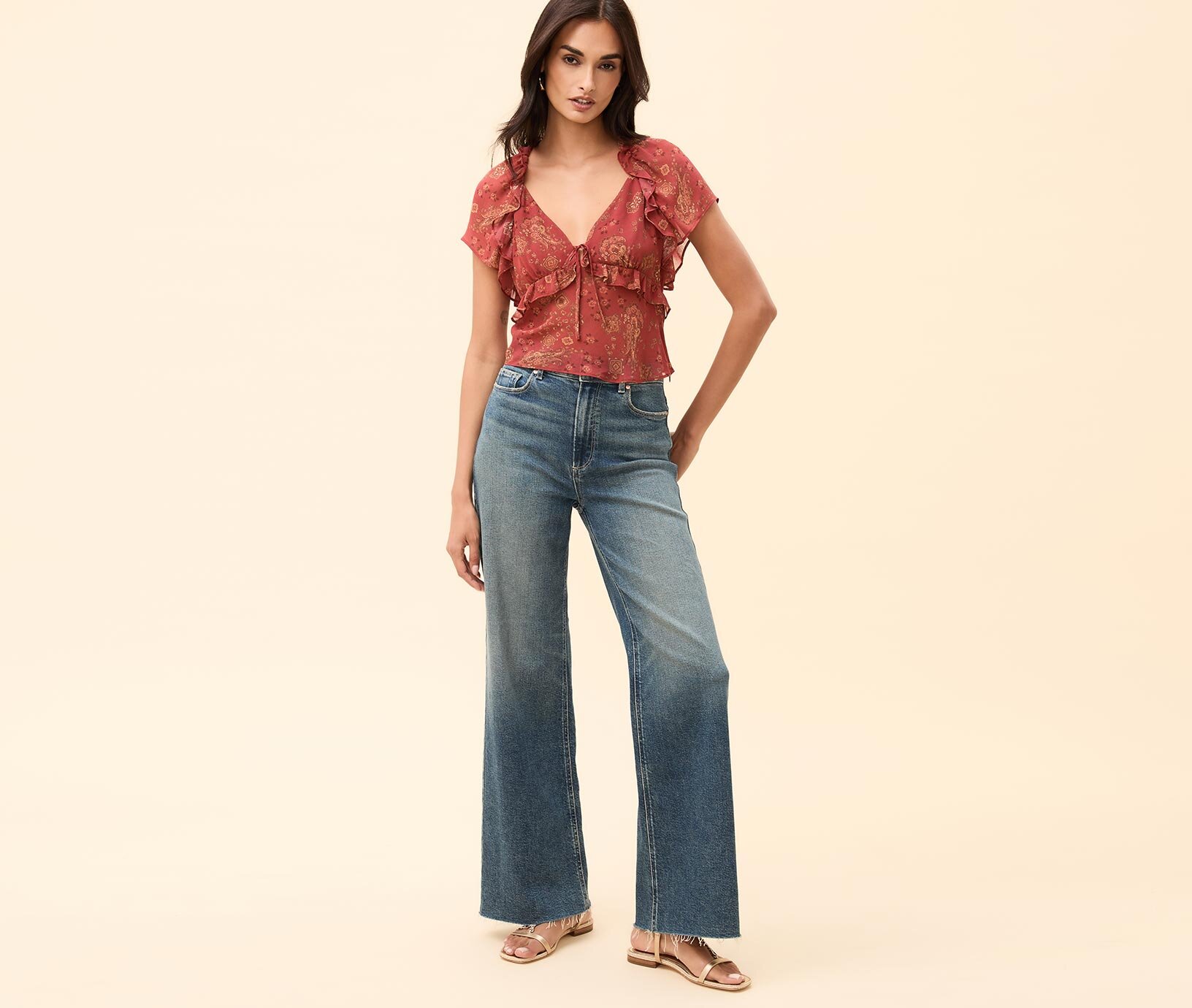 Woman wearing a red paisley printed short sleeve blouse, dark wash wide leg denim and gold flat sandals