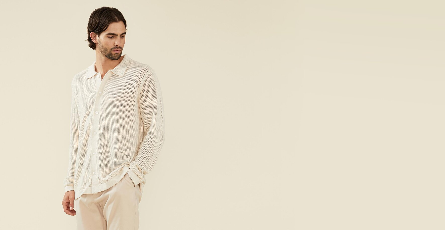 Man wearing an ivory open knit button up sweater and cream trousers